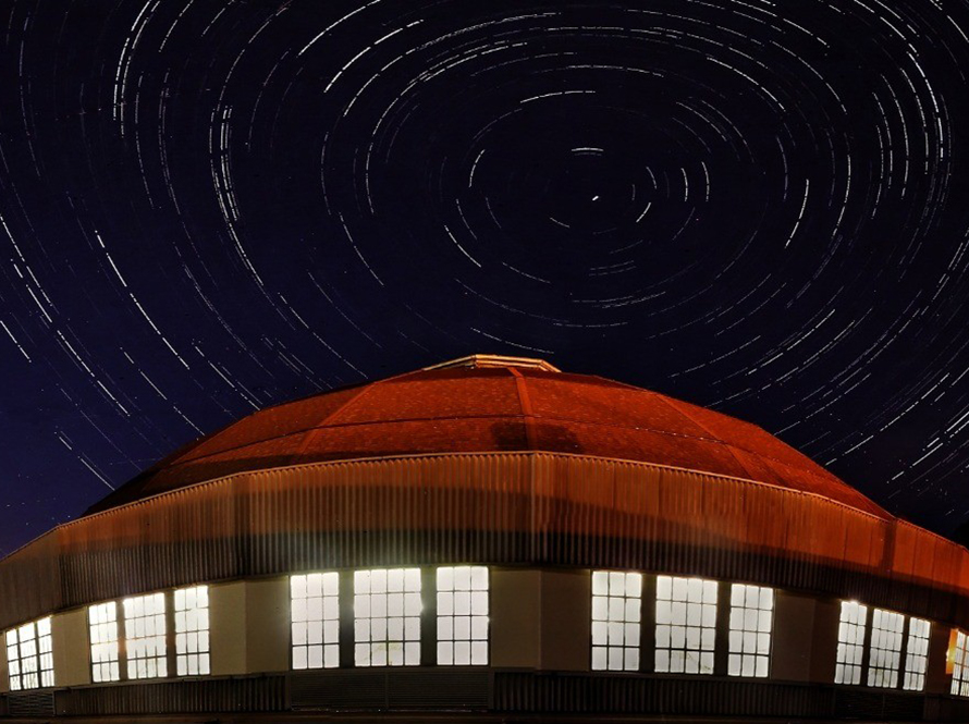 Time-lapse photo of the night sky behind a round red-roofed building