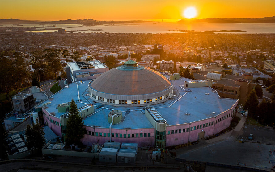 Arial view of a round building with a domed roof with the bay in the background at sunset
